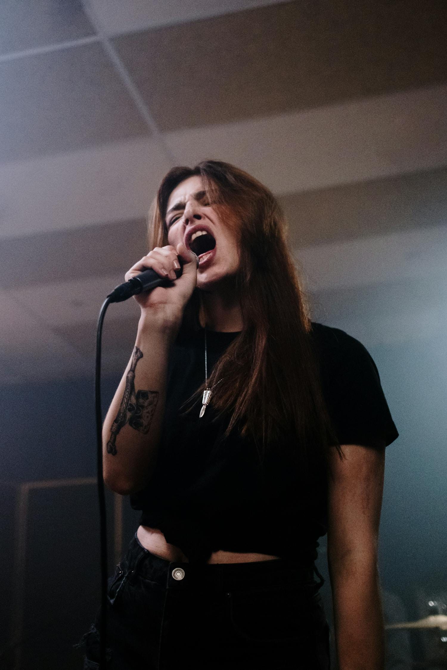 A passionate female singer in a black shirt performs intensely with a microphone indoors.