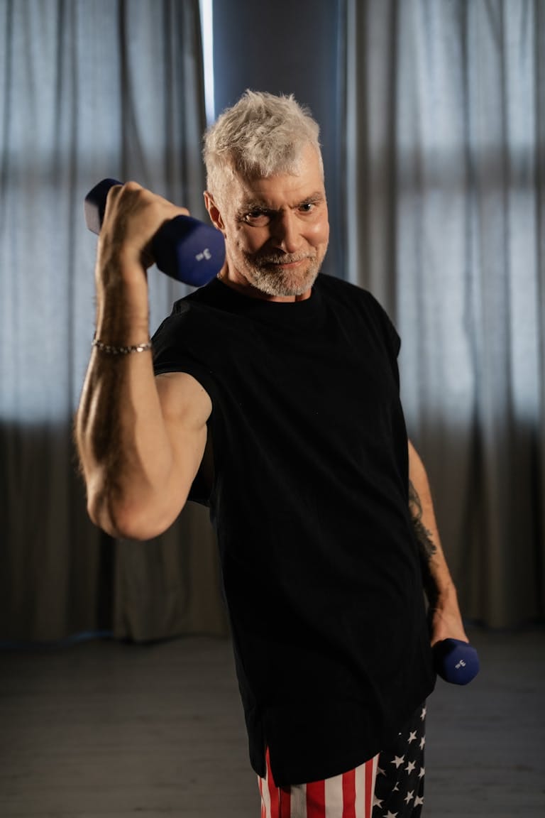 Energetic senior man working out with dumbbells indoors, promoting positive aging and wellness.